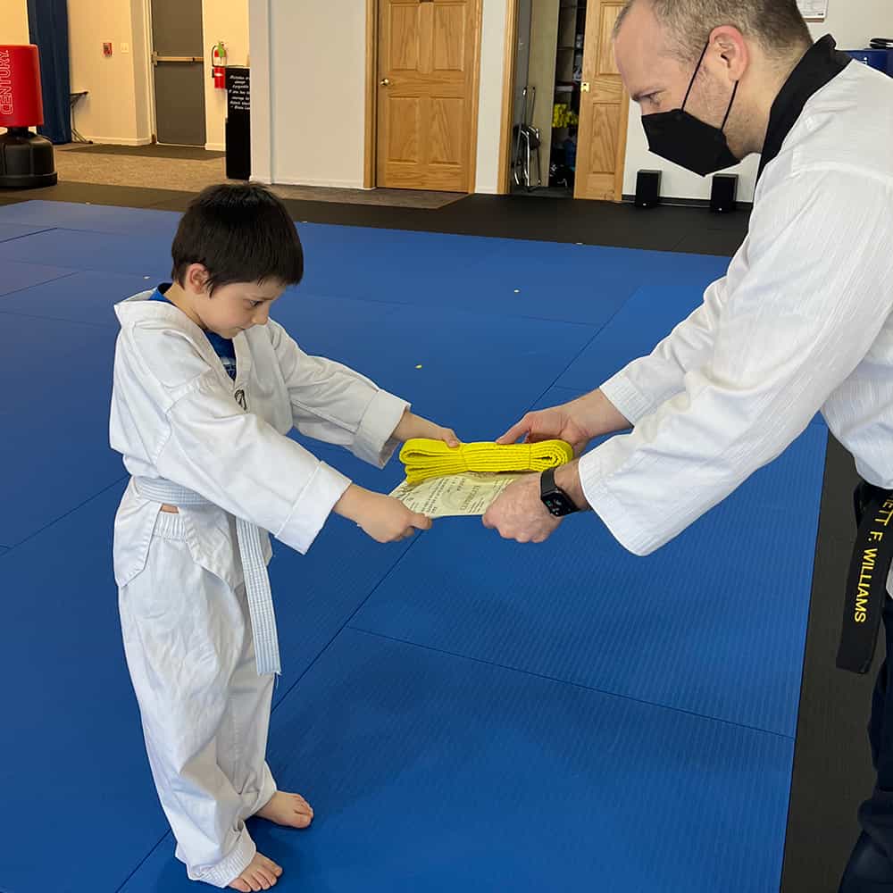 Student bowing to show respect while receiving new belt in kids class